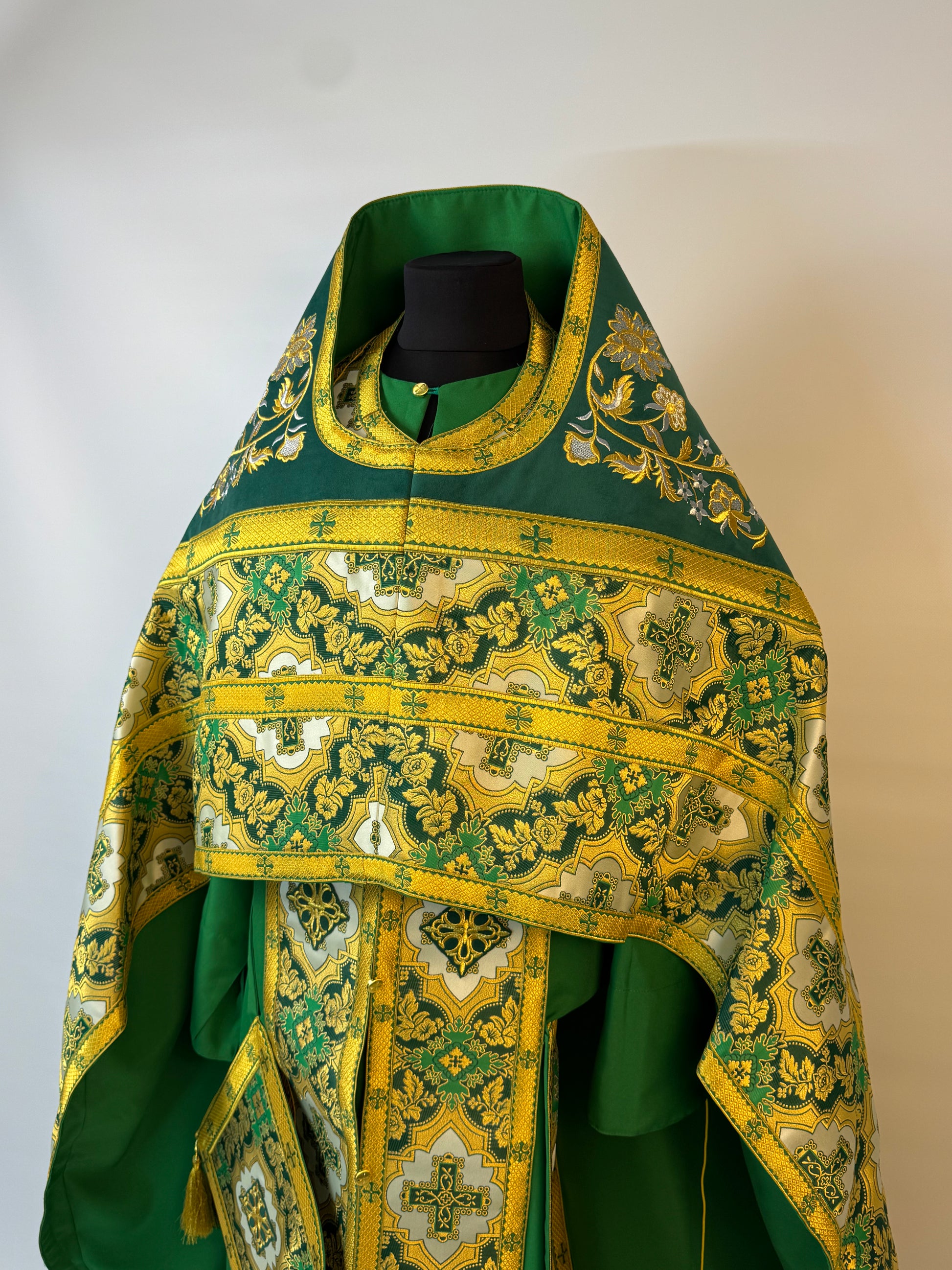 Green and gold embroidered religious vestment on a mannequin against a white background