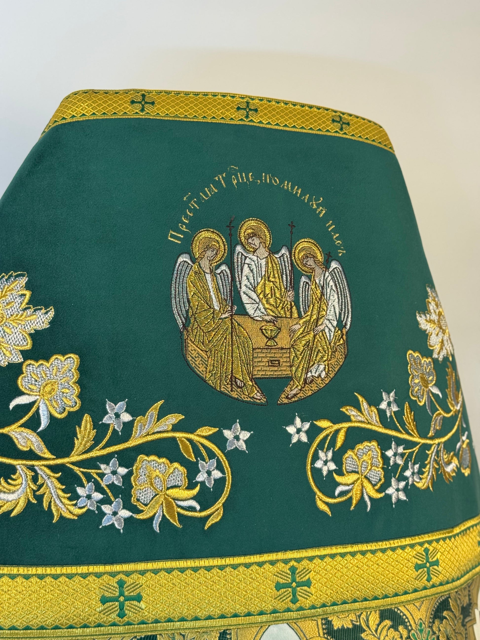Embroidered green fabric with gold and white floral patterns and angelic design on a white background